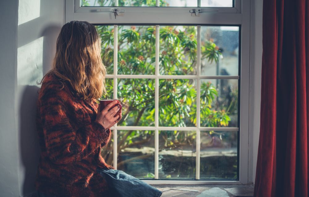 Woman sitting at the window with a view of lively greenery while she is sipping a cup of menopause tea