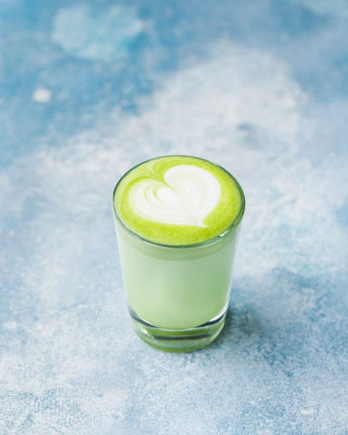 
                    
                      Blueberry Matcha Organic drink with heart latte art in a clear glass on a blue background.
                    
                  