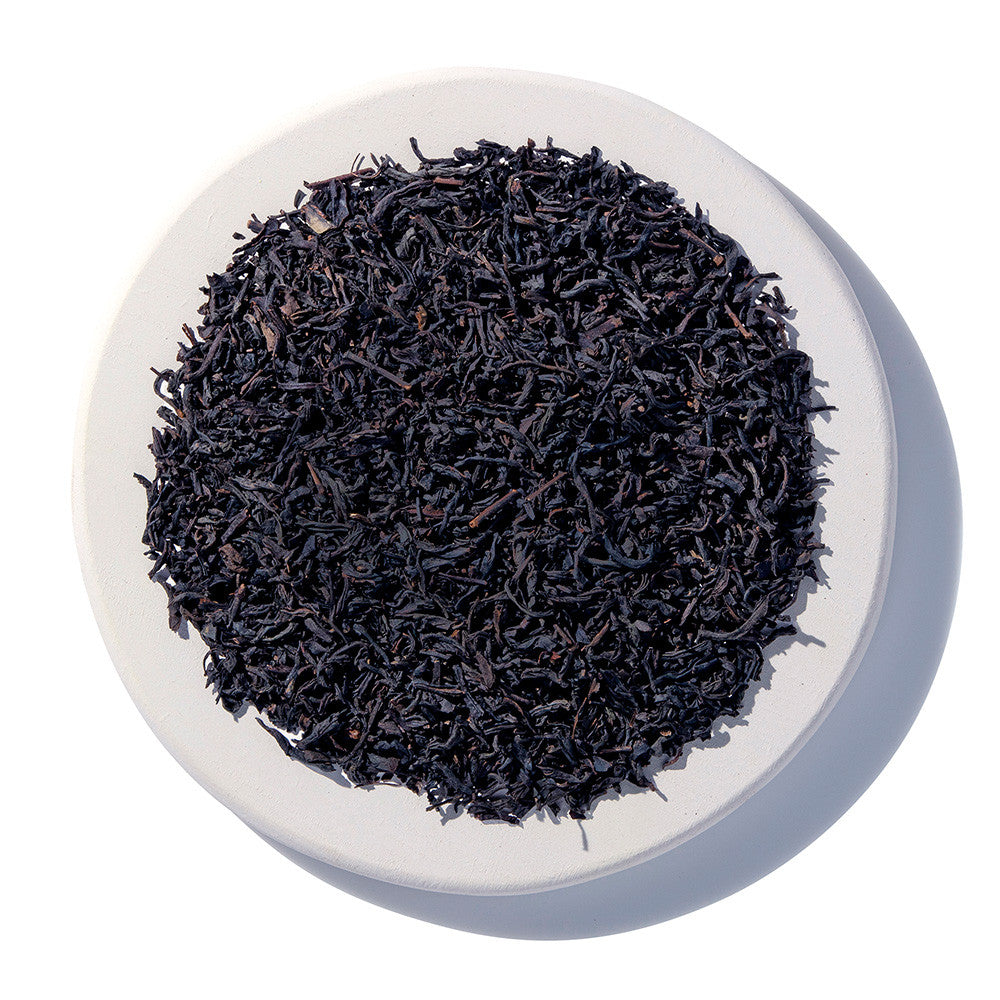 Black tea leaves in a white bowl on a white background